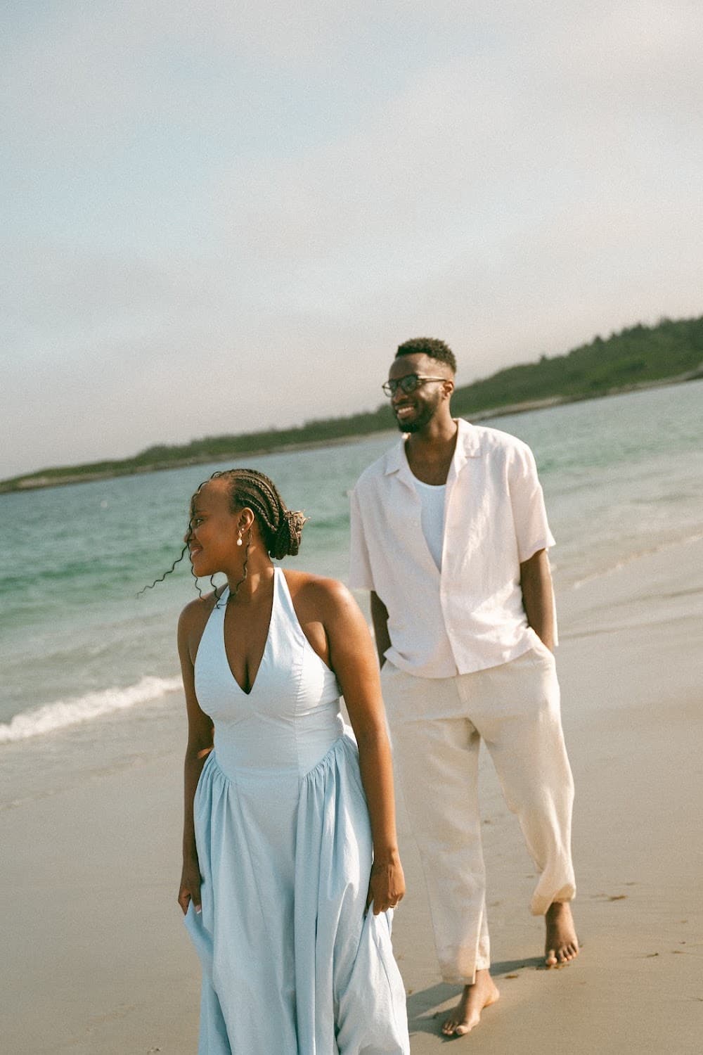 Joshua and Sandrine walking along the beach in white