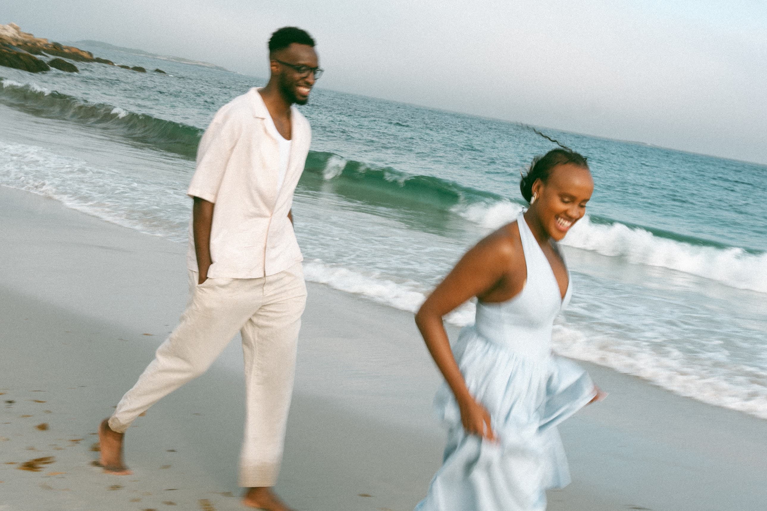 Joshua and Sandrine laughing as they run along the beach in white